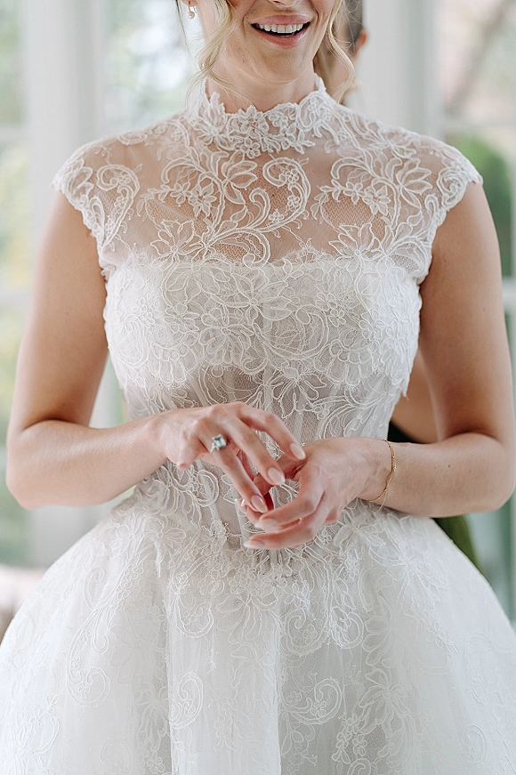 Wedding dress with high neck lace bodice and sheer illusion neckline, cap sleeves, and bridal earrings in bright window light indoors