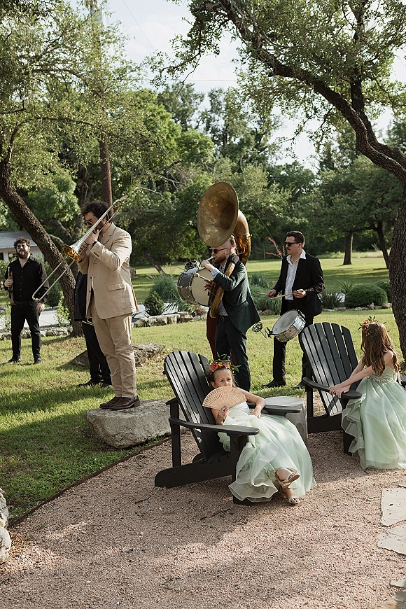 Wedding band performance with a brass band wedding playing trombone and sousaphone as kids in green dresses watch on a garden lawn