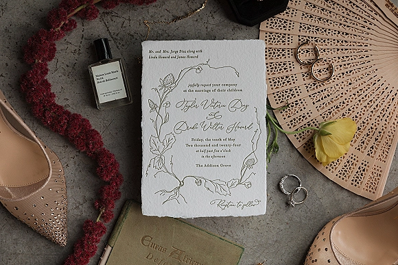 Wedding invitation suite with a deckle edge wedding invitation, botanical line art, rose gold rings, blush heels on gray stone surface