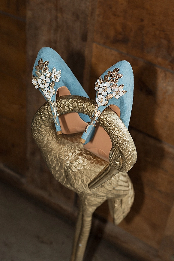 Bridal shoes in blue wedding shoes style, powder blue suede heels with floral clips and gold leaf details beside a gold swan sculpture