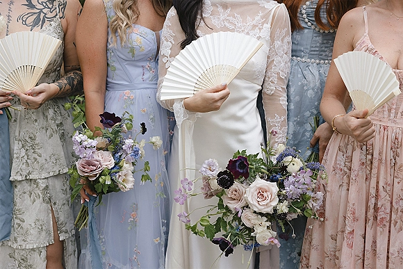 Bridal party portrait of bride with bridesmaids holding bouquets, wearing lace sleeves and mix-and-match dresses in outdoor greenery