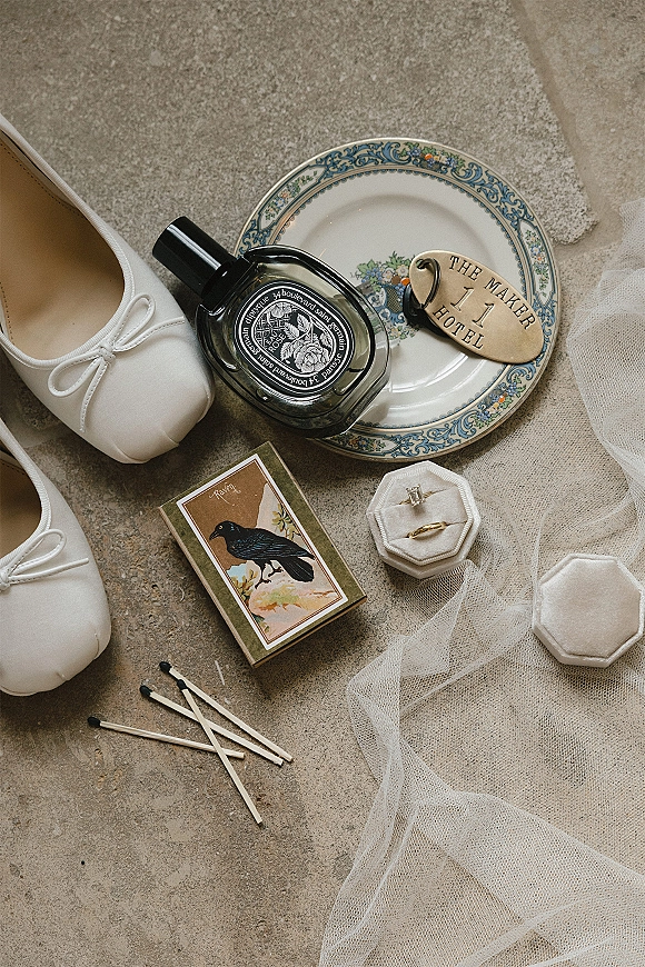 Wedding details flat lay with wedding rings in a ring box, bridal shoes, perfume, vintage plate, and veil on a stone floor