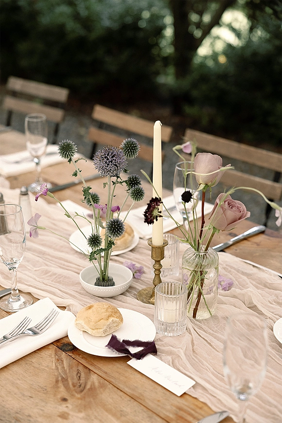 Wedding tablescape with rustic wedding table styling, gauze runner, blush roses, taper candles, and place cards in a garden setting