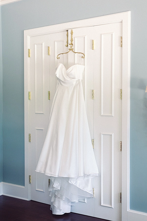 Wedding dress, strapless wedding dress hanging on a hanger against closet doors, with a blue wall and wood floor below