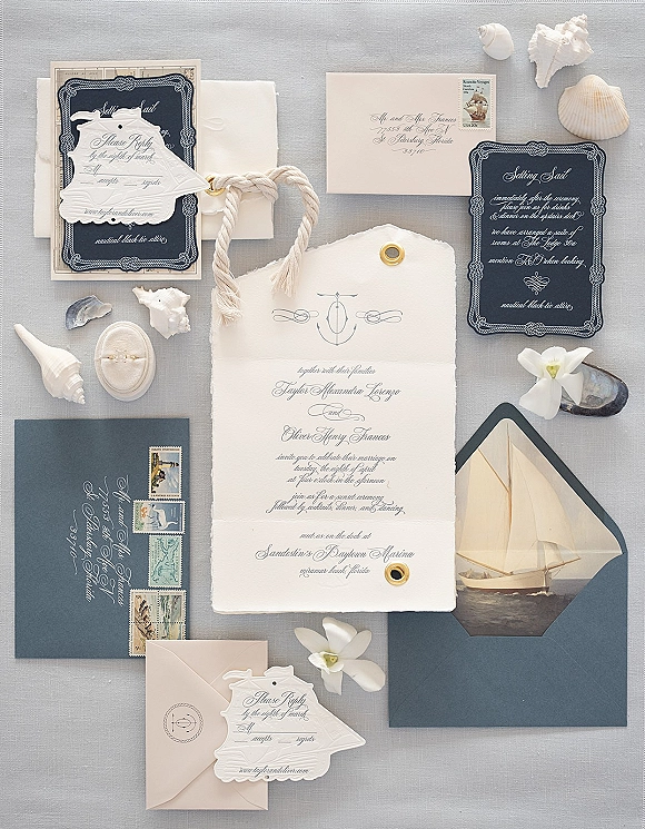Invitation suite with navy and white wedding invitations, deckle edge paper, stamps, rope cord, ring box and seashells on linen backdrop