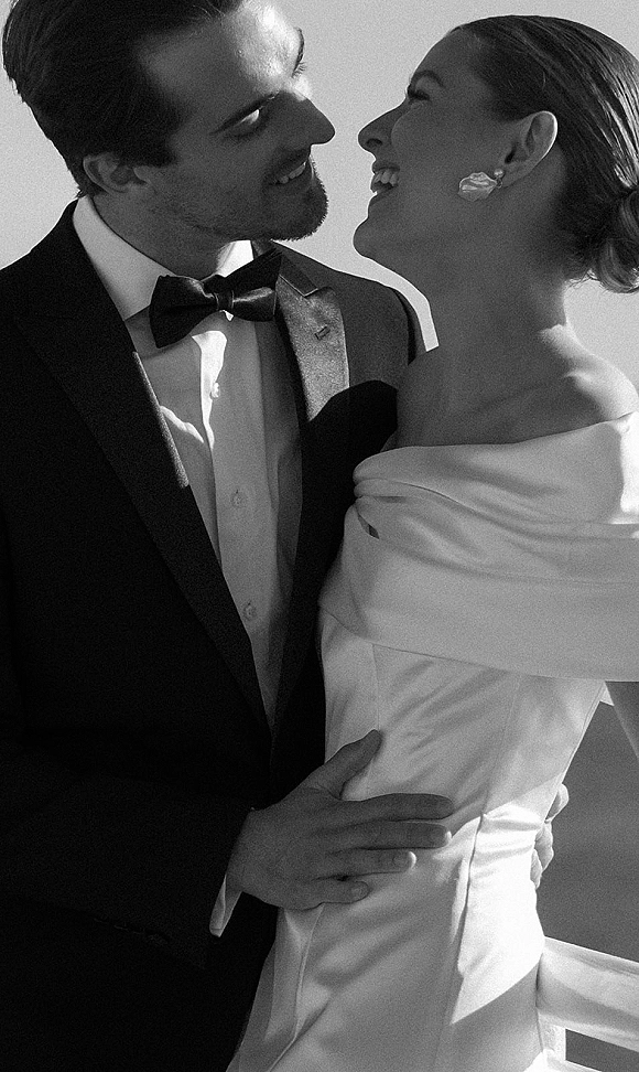 Couple portrait in a black and white wedding portrait style, bride and groom close up laughing and embracing against a plain wall