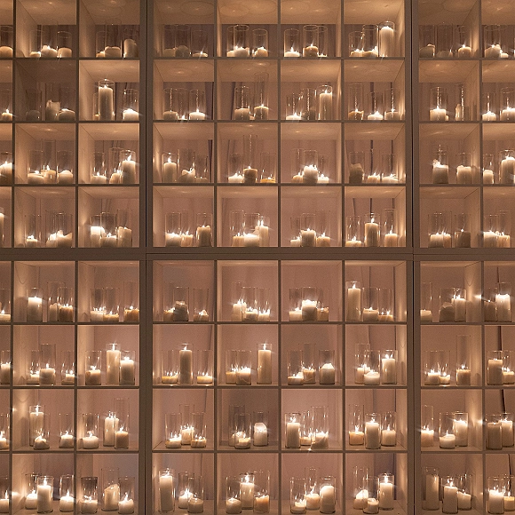 Wedding candle wall candle wall backdrop with pillar candles in glass hurricane vases on a grid shelving display under warm indoor lighting