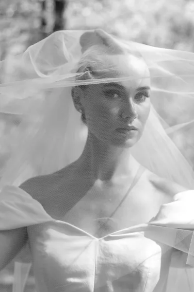 Bridal portrait with veil over face, a bride in an off-the-shoulder gown, sheer tulle draped across her shoulders, features softly obscured.