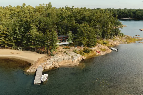 Lakeside ceremony setup for a beach wedding ceremony, a floral arch fronts calm lake water with pine trees and a dock with boats along the shore.