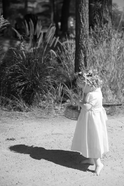 Flower girl portrait of an outdoor flower girl wearing a flower crown along a dirt path framed by tall grass and trees.