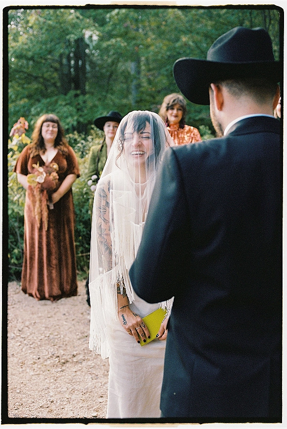 Wedding vows during an outdoor wedding ceremony as bride and groom face each other, groom in black cowboy hat on a forest gravel path