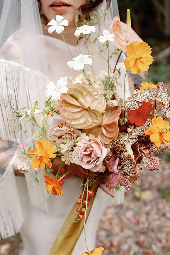 Bridal bouquet, tropical bridal bouquet with anthurium, orchids, roses and cosmos, tied with ribbon, held against blurred outdoor greenery