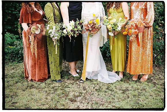 Bridesmaid bouquets in mixed wildflower bouquets style held by women in mismatched dresses, long ribbons draping over heels on a garden lawn