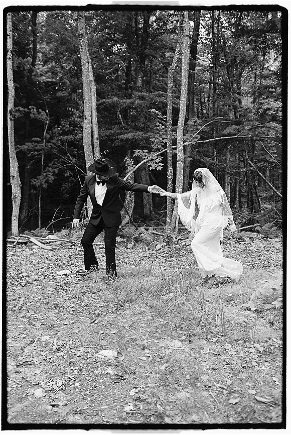 Couple portrait, black and white wedding portrait of bride and groom holding hands on a forest path, groom in cowboy hat and veil flowing
