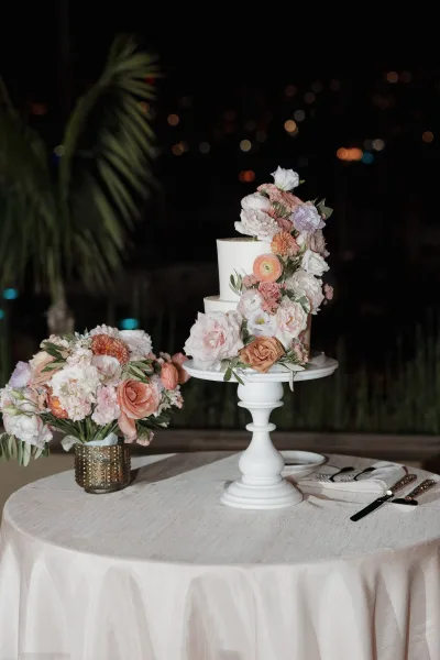 Wedding cake two tier wedding cake with white buttercream and fresh flower topper on a styled table under bokeh lights outdoors at night