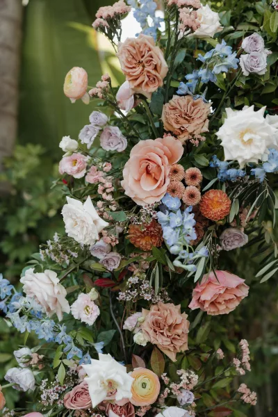 Wedding floral arrangement with roses and ranunculus in soft pastel tones on a ceremony floral pillar, set against blurred garden greenery