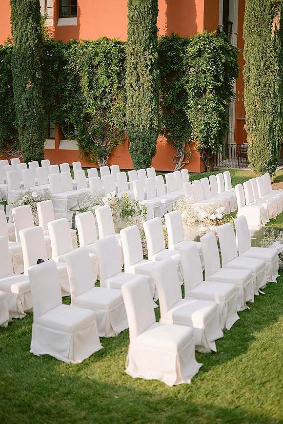 Ceremony seating with outdoor ceremony seating, rows of white chair covers lined along an aisle with baby's breath and greenery on grass lawn