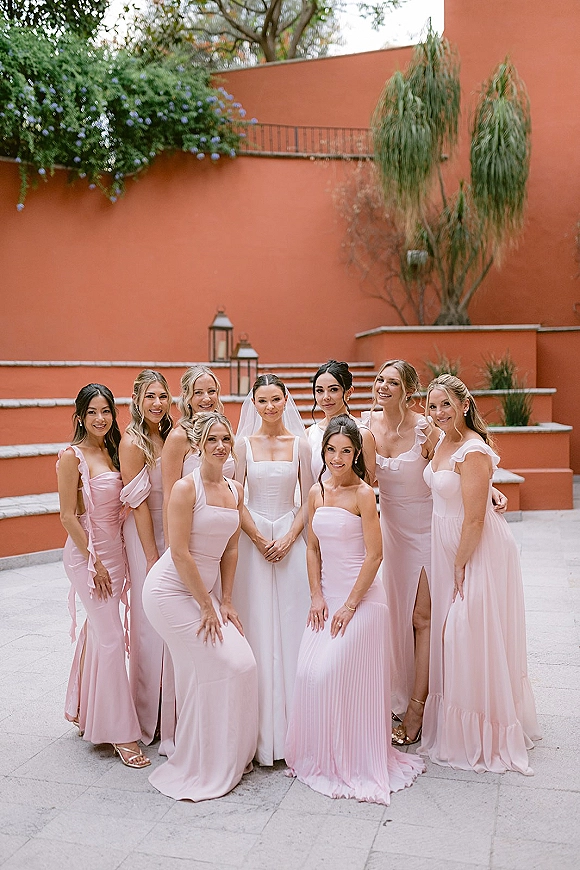 Bridesmaid group photo with bride centered, bridesmaids in blush pink dresses on stone steps by a terracotta wall in courtyard setting