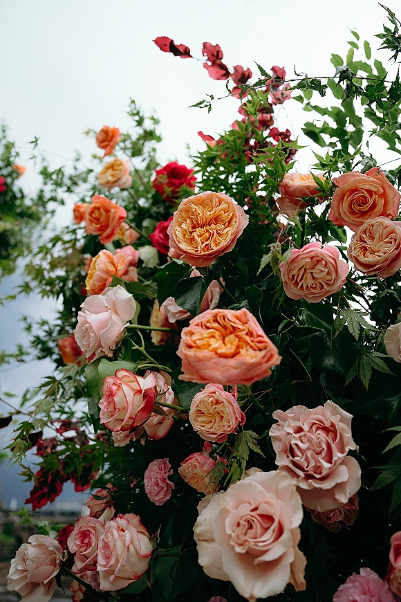 Wedding floral arrangement on a ceremony arch with garden roses and greenery foliage, framed by open sky and distant landscape