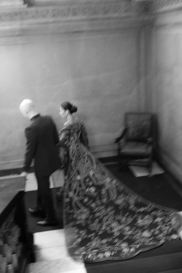 Reception entrance as bride and groom walk together, her long sleeve embroidered gown train flowing in a grand paneled staircase interior