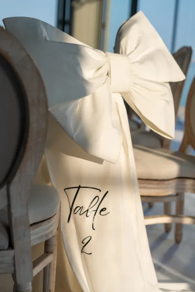 Wedding chair decor highlights a neat chair bow with a single table number sign, balanced for a modern neutral look.