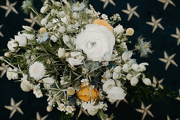 Bridal bouquet wildflower bridal bouquet with white ranunculus, chamomile daisies, thistle, yellow blooms, and ribbon on dark starfish fabric