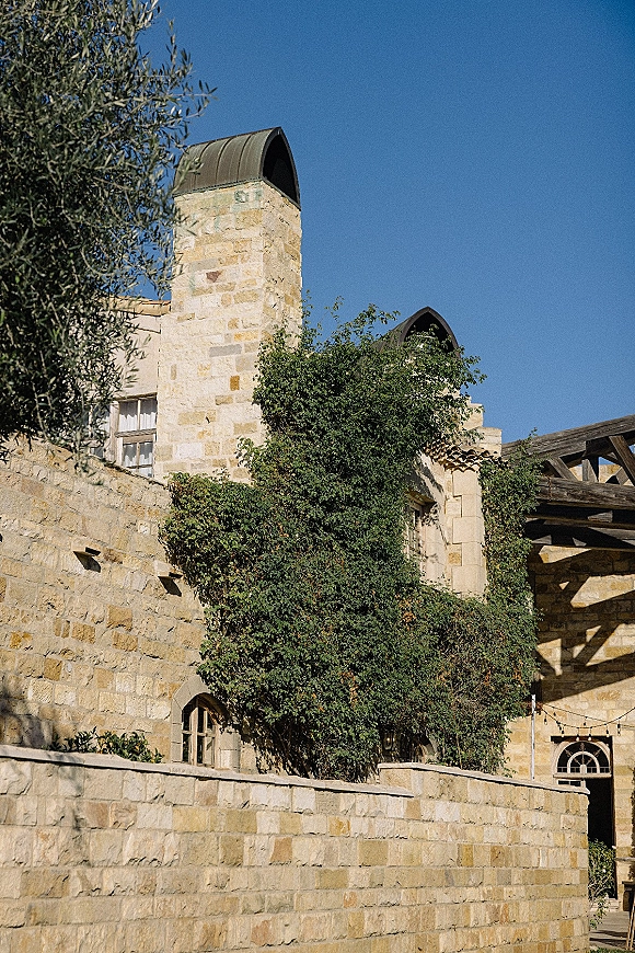 Wedding venue exterior with ivy vines on a stone wedding venue facade, wooden pergola and string lights under a blue sky