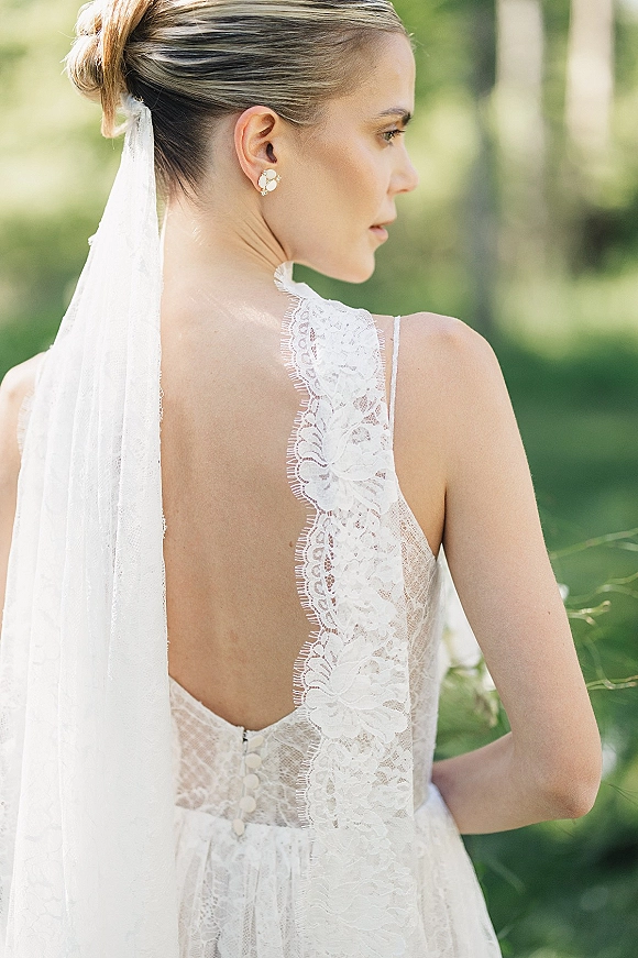 Bridal portrait of a bride in side profile wearing a backless lace wedding dress, looking over her shoulder in soft sunlit greenery