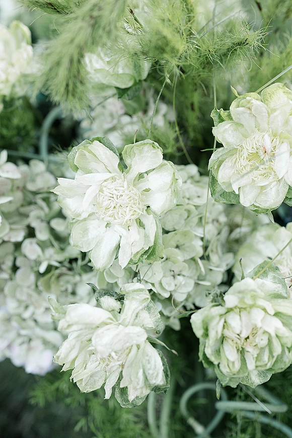Wedding floral arrangement of white wedding flowers with lush greenery accents, photographed close up against softly blurred garden leaves