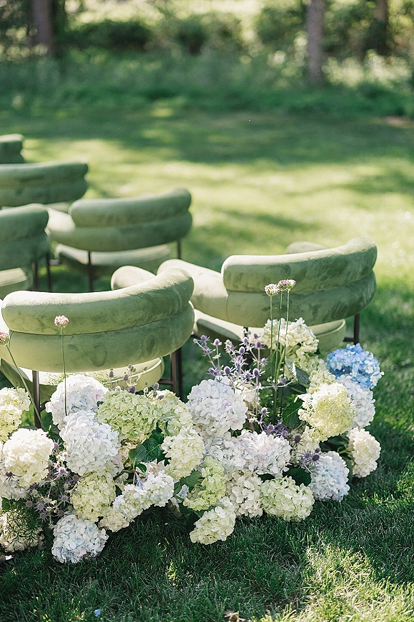 Outdoor ceremony seating with garden wedding ceremony chairs in green velvet, lined by hydrangeas on a sunlit lawn among trees