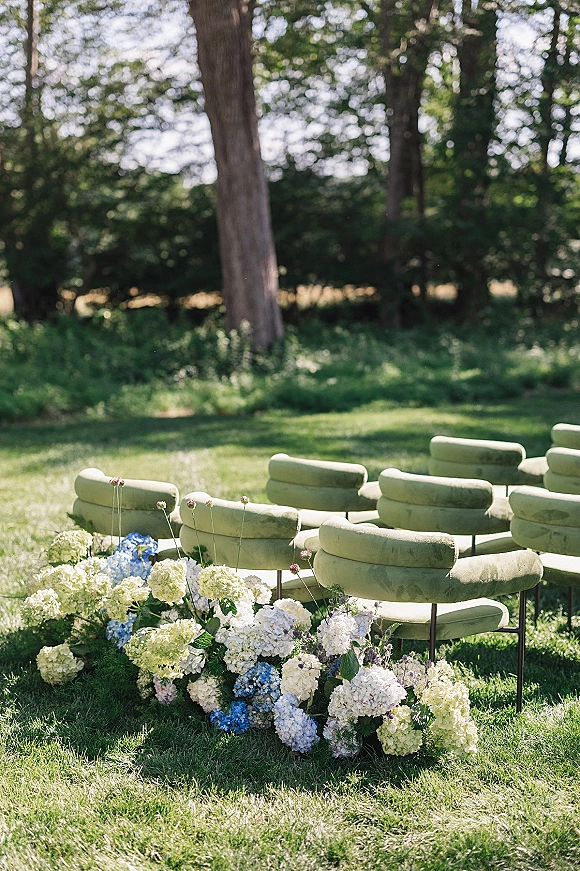 Ceremony seating with outdoor wedding ceremony seating in green chairs lining a grassy aisle, bordered by hydrangea flowers in sunlight