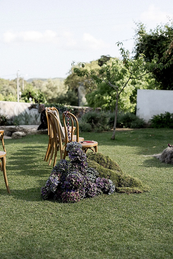 Ceremony aisle decor with outdoor wedding aisle chairs, woven wood seating beside a mossy purple hydrangea ground arrangement on a lawn