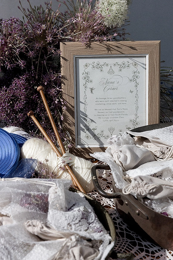 Wedding sign in a wooden frame with wildflowers, yarn and knitting needles, lace fabric and blue ribbon, set outdoors near water