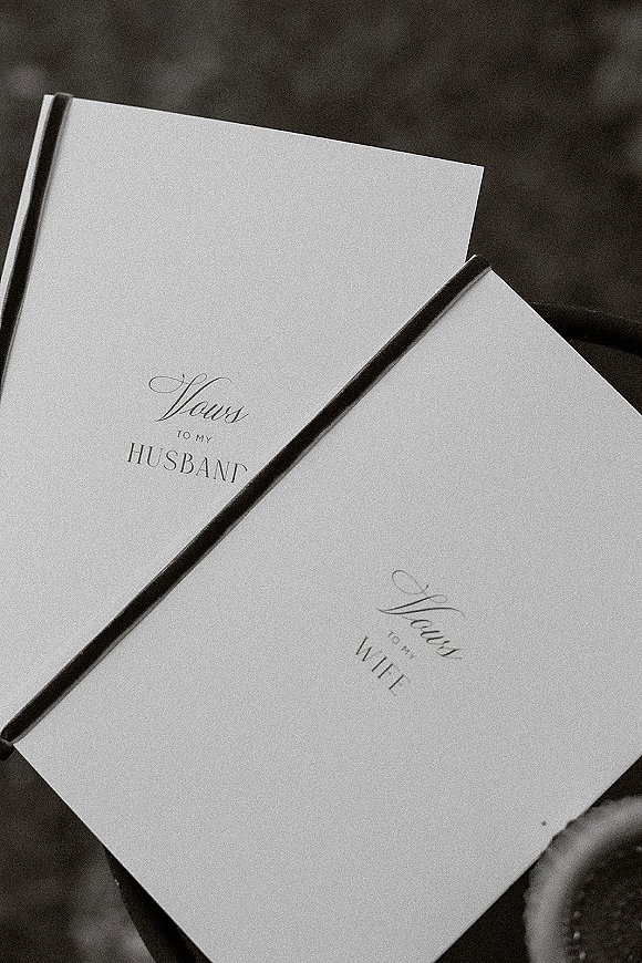 Wedding vows book with calligraphy lettering and a black ribbon bookmark resting on a dark fabric surface, elegant wedding stationery detail
