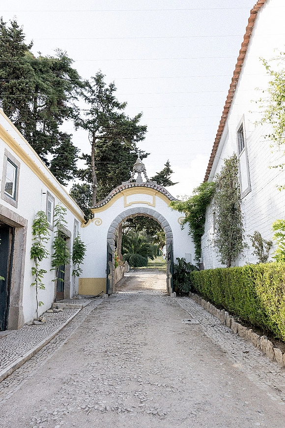 Wedding venue entrance with an estate archway entrance, stone arch and wrought iron gate framing a cobblestone courtyard lane with vines and hedges