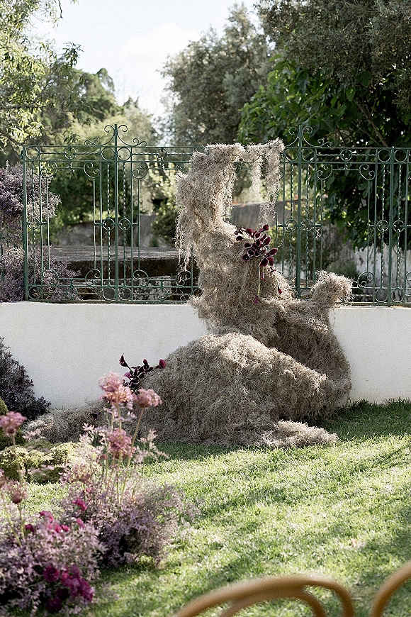 Wedding ceremony arch with moss and dark purple orchids in an asymmetrical floral arrangement on a garden lawn by stone steps