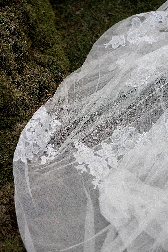 Bridal veil with lace wedding veil appliqué and tulle spread on mossy grass, highlighting delicate floral stitching and sheer fabric texture