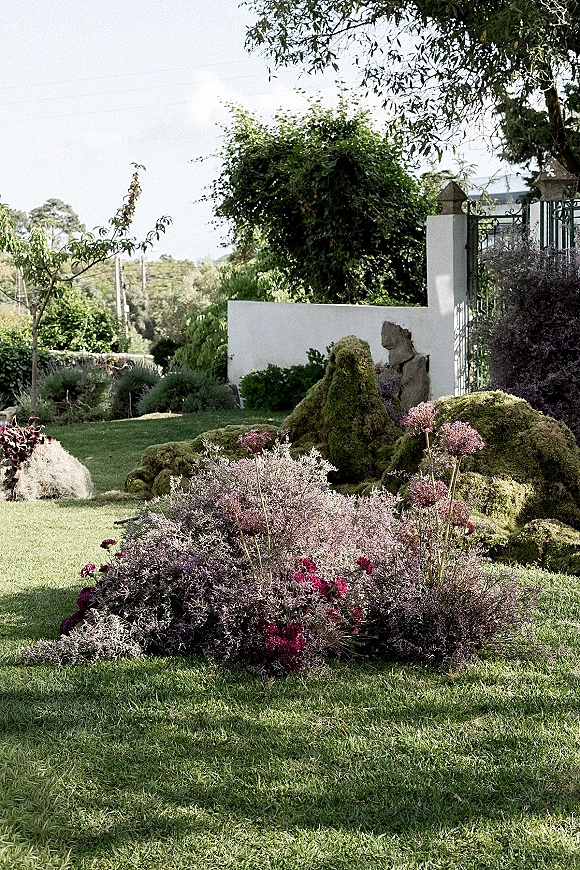 Outdoor wedding florals with ceremony ground florals featuring purple blooms, tall stems, and greenery nestled among mossy rocks on a lawn