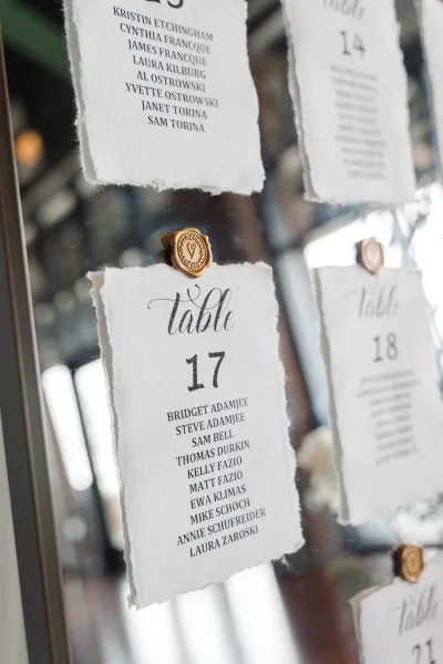 Seating chart on a mirror wedding sign with wax seals, reflecting windows and warm interior lights in the background.