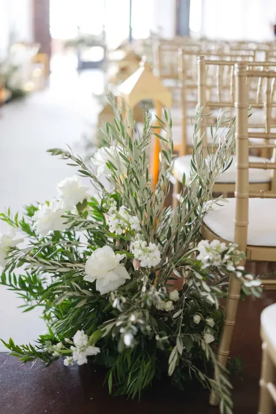 Ceremony aisle decor with graceful aisle floral arrangements, accented by lanterns along a window-lined indoor aisle.