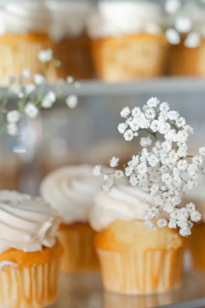 Wedding cupcakes, styled as buttercream swirl cupcakes with a sprig of baby's breath, displayed on a glass shelf.
