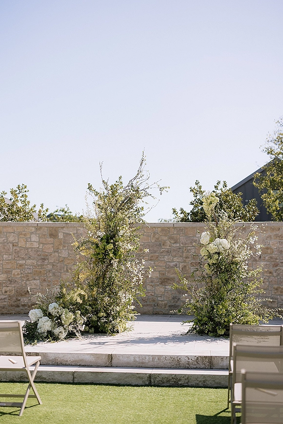 Ceremony altar decor with asymmetrical wedding altar flowers in white hydrangeas and greenery, set before a stone wall on an outdoor patio