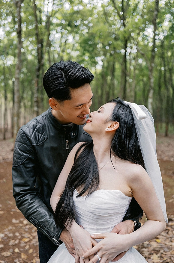 Wedding couple portrait of bride and groom embracing with a bridal veil accent on a tree-lined forest path with fallen leaves