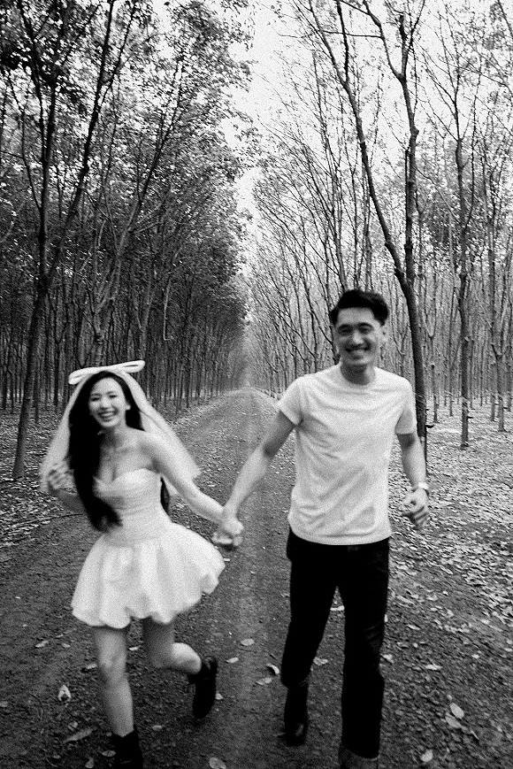 Couple portrait holding hands and running down a tree-lined forest road, bride in short wedding dress with veil bow amid fallen leaves