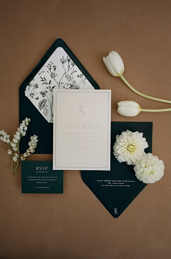 Wedding invitations in a modern wedding invitation suite with black envelopes and white tulip accents on a brown paper backdrop