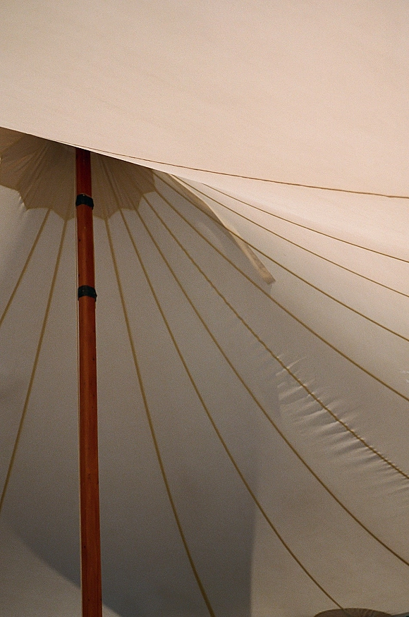 Tent ceiling decor in a wedding tent interior with canvas sailcloth canopy, wooden center pole, wrapped supports, and visible roof lines