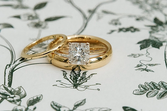 Wedding rings with gold wedding bands and a solitaire diamond engagement ring resting on white paper with botanical illustration details