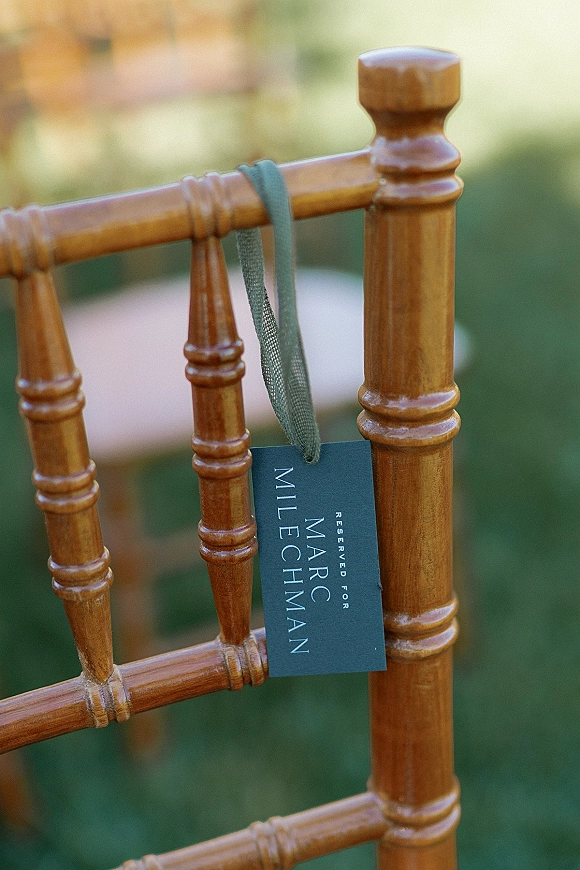 Wedding chair tag with a reserved wedding chair sign tied by ribbon to a wood chiavari chair on an outdoor lawn with blurred greenery