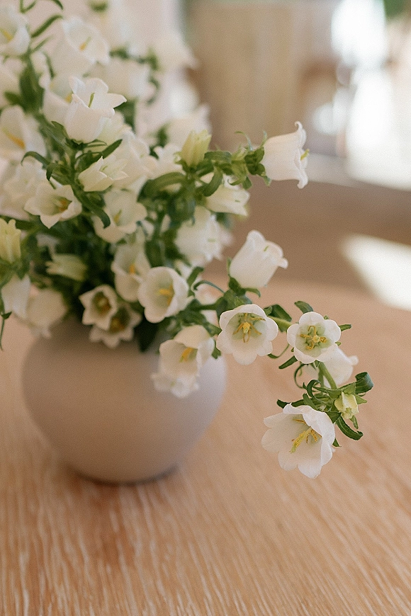 Wedding centerpiece flowers in a simple arrangement of white flowers and greenery in a vase on a wood table in soft indoor light