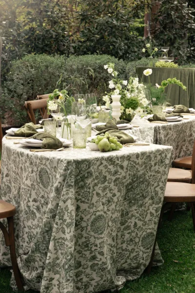 Reception tablescape with green wedding tablescape details, patterned tablecloth, white florals, gold flatware, fruit, and green votives on a lawn